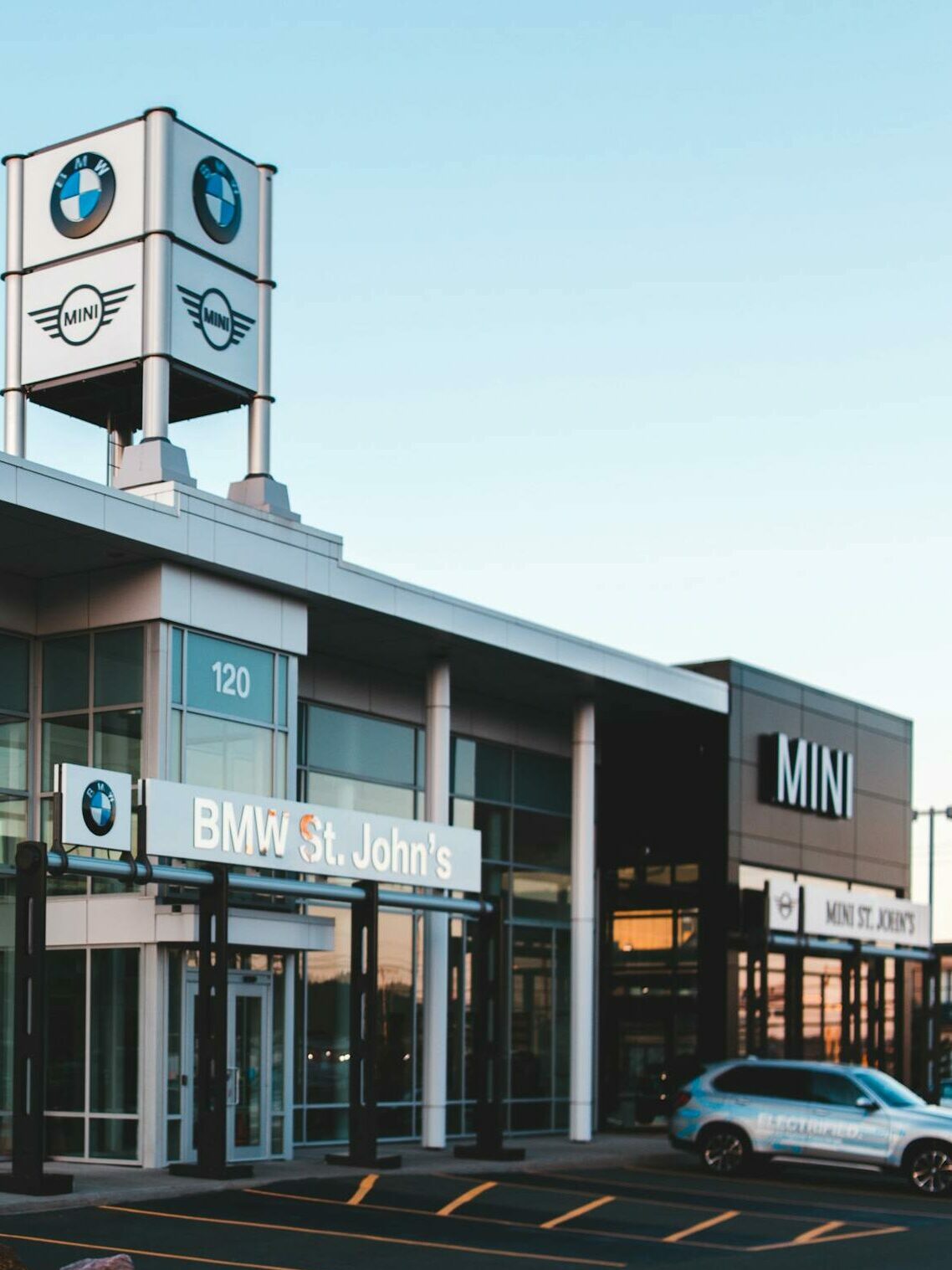 Luxurious car dealership showcasing BMW and MINI cars with a modern glass exterior at dusk.