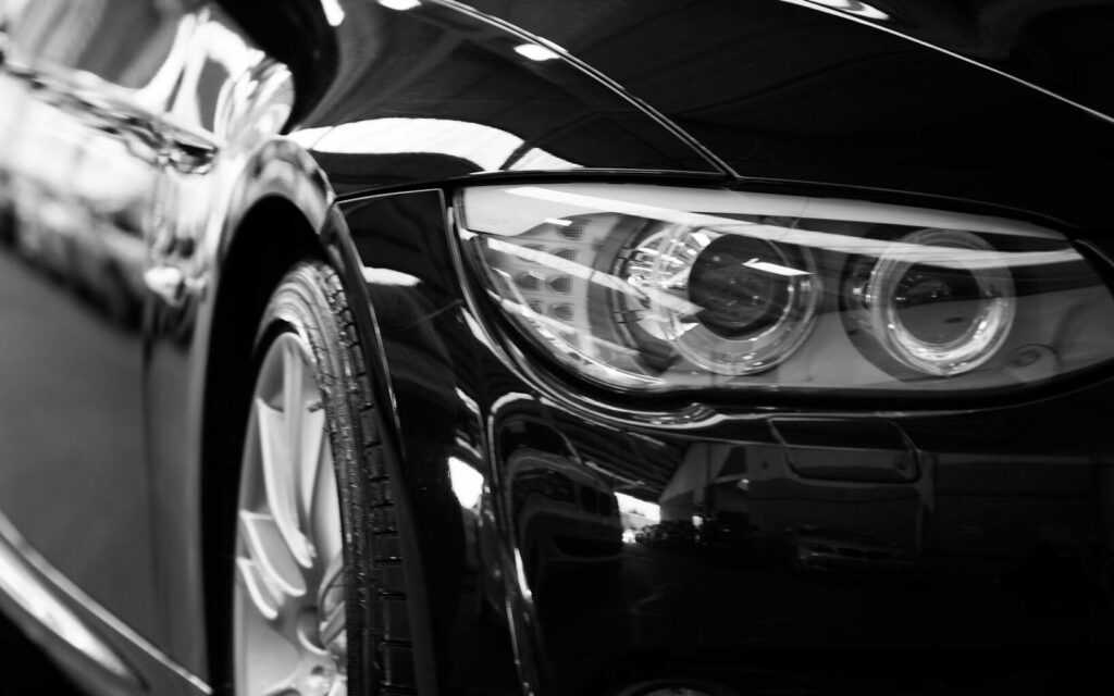 Close-up black and white image of a luxury car line-up focusing on vehicle headlights.