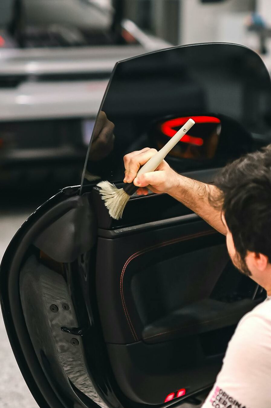 A mechanic meticulously cleaning a car door in a professional workshop setting, showcasing care and precision.