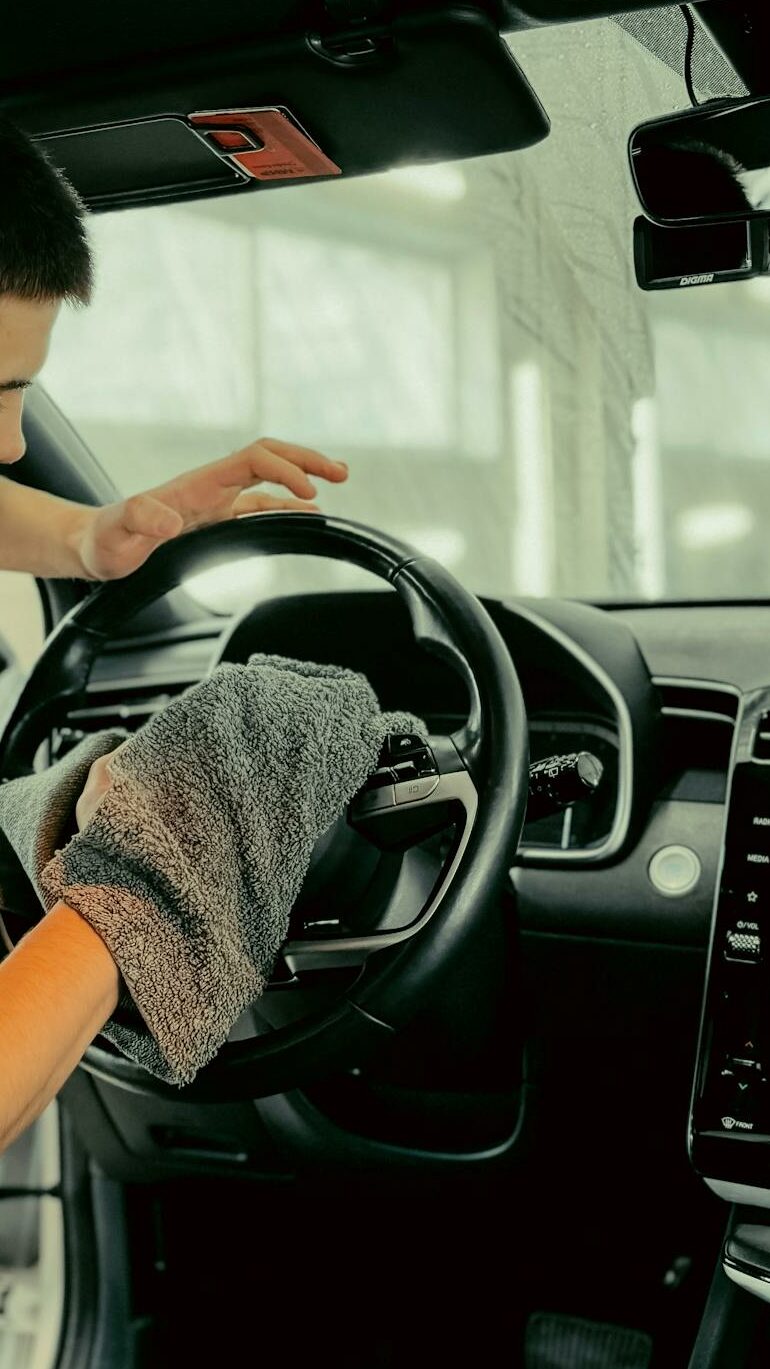 Young man polishing car steering wheel with cloth, ensuring clean interior.